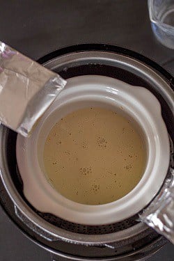 The Instant Pot breakfast pudding is lowered into the Instant Pot after placing a foil sling.