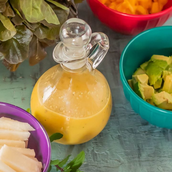 A glass cruet of passion fruit dressing with salad ingredients.