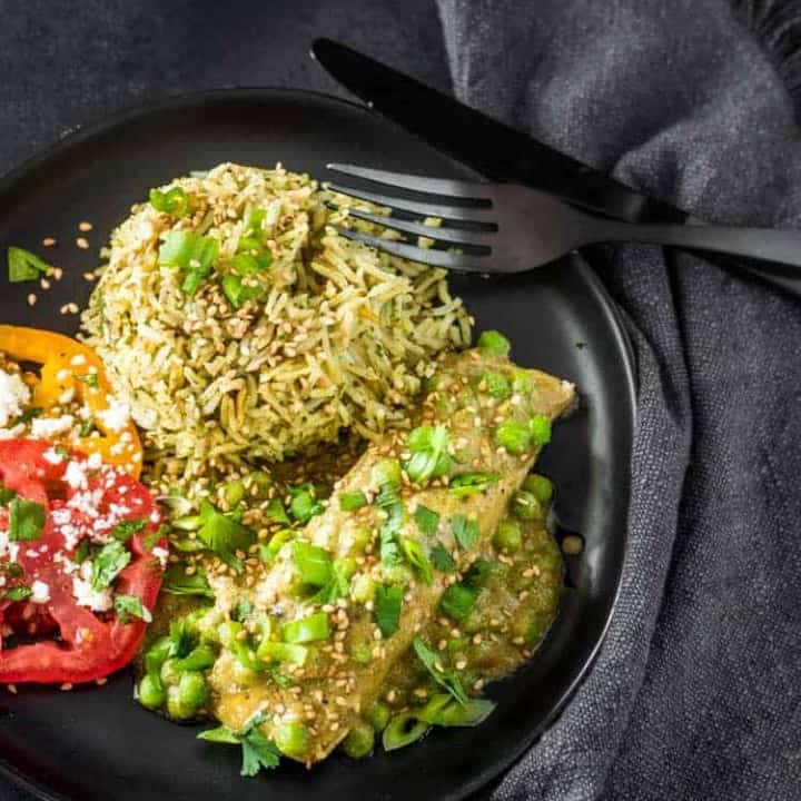 Salmon in Quick Mole Verde with cilantro rice and sliced tomatoes on a black plate with black flatware