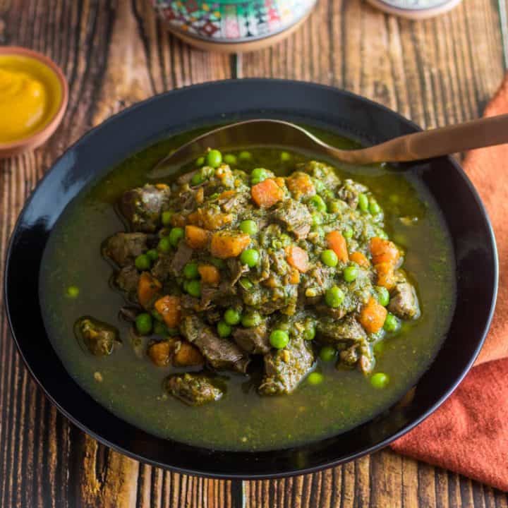 A bronze ceramic bowl of Slow Cooker Peruvian Lamb Stew (Seco de Cordero) - tender lamb chunks, veggies, and a savor cilantro-aji amarillo broth with a copper spoon, a Peruvian salt dish, and a tiny bowl of aji.