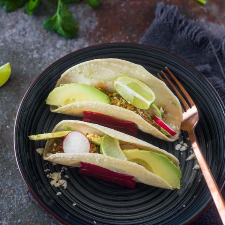 A grey ceramic plate with 2 chorizo and eggs breakfast tacos and a copper fork.