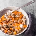 A speckled grey bowl of dragon fruit salad with tajin and lime dressing with a silver serving spoon and a grey napkin.