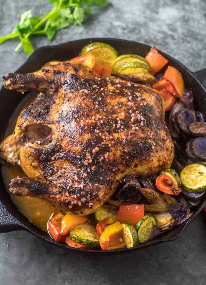 Mexican Roasted Chicken and Vegetables in a black cast iron skillet with cilantro garnish on a grey background.