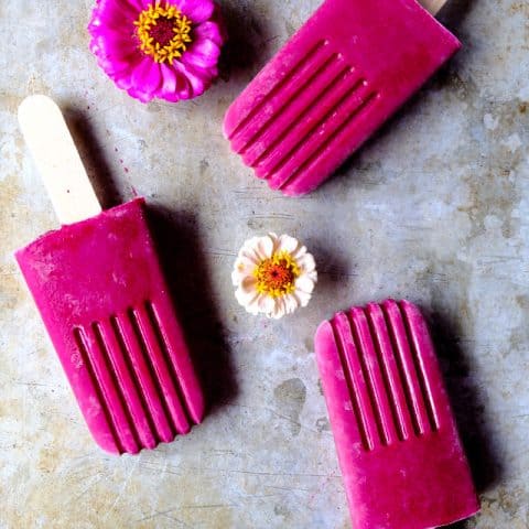 strawberry beet smoothie pops on a grey background with flowers.