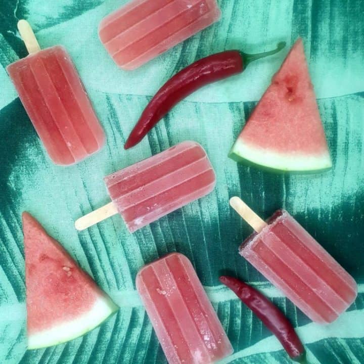 watermelon chile popsicles on banana leaves with red chiles.