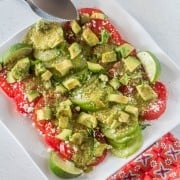 A white square plate with tomato and tomatillo salad with cilantro-lime dressing, tongs, print napkin.
