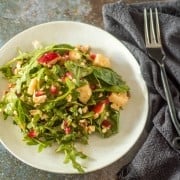 A white round plate with an arugula salad tossed with chamoy vinaigrette.