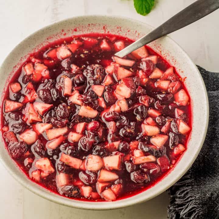 A white bowl of pear and cranberry sauce with orange liqueur and a silver serving spoon.