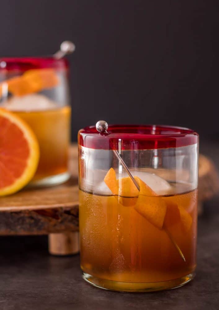 An orange pomegranate manhattan variant in a rocks glass with orange twist garnish.