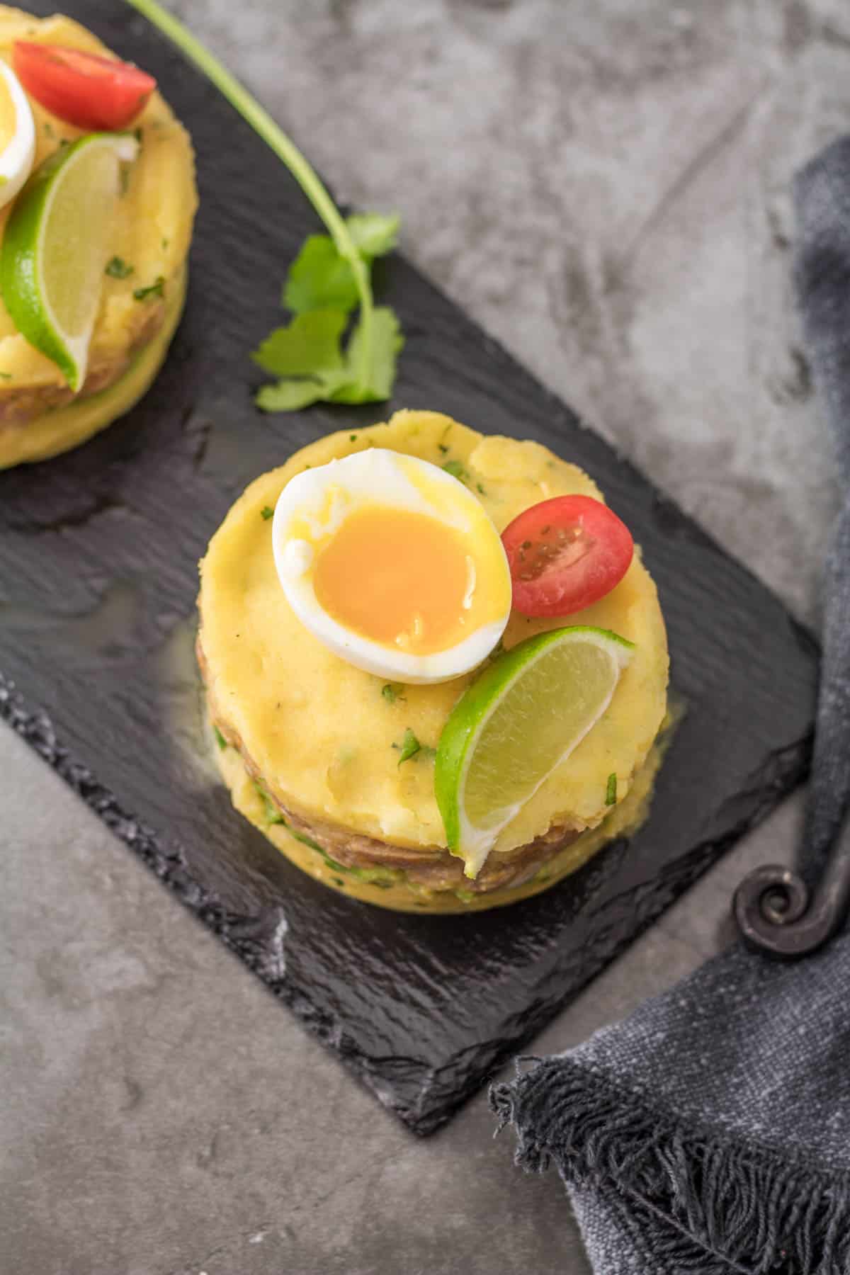 A bird's eye view of a tuna causa with a soft-boiled egg on a slate tray.