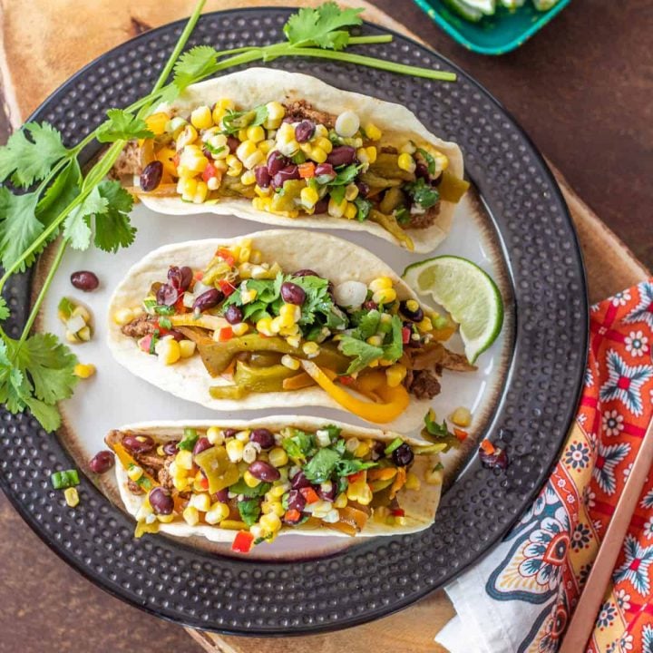 A bird's eye view of 3 pork fajita tacos with cilantro and lime on a plate.