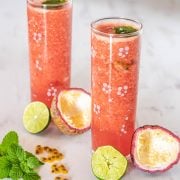 Tall glasses of agua fresca, 2 squeezed lime halves, 2 passionfruit halves with pulp removed.