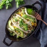 A close up of a cast iron dish with 3 nopales tacos topped with corn, onions, avocados, cotija, and cilantro.