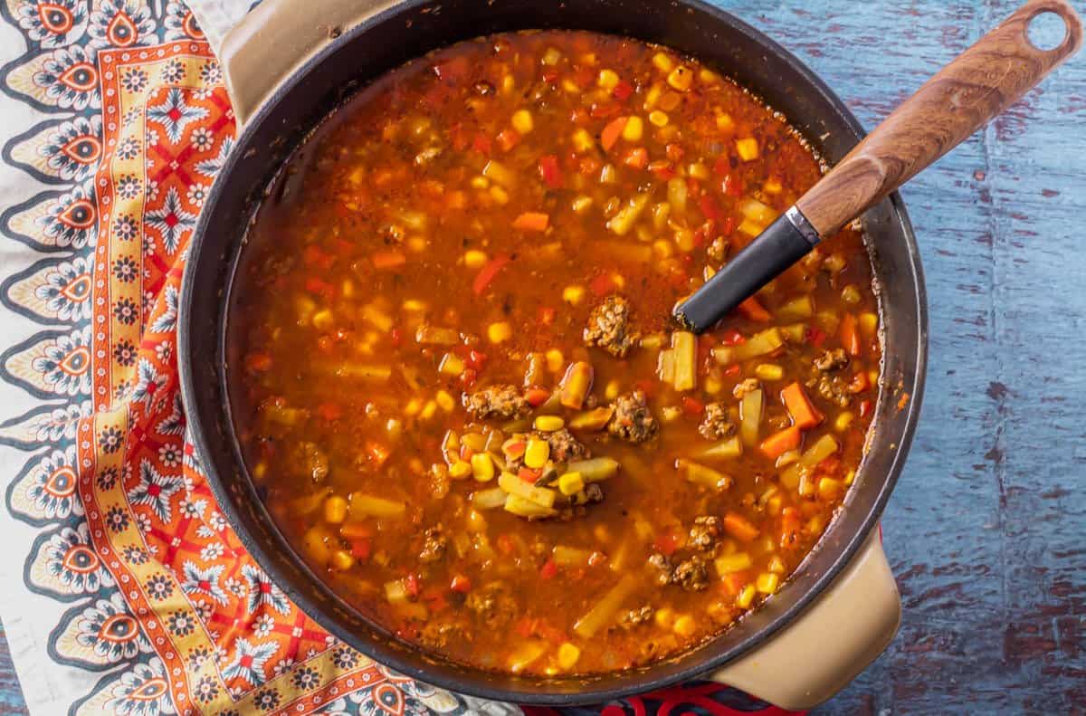 A cast iron dutch oven with picadillo soup and a ladle.