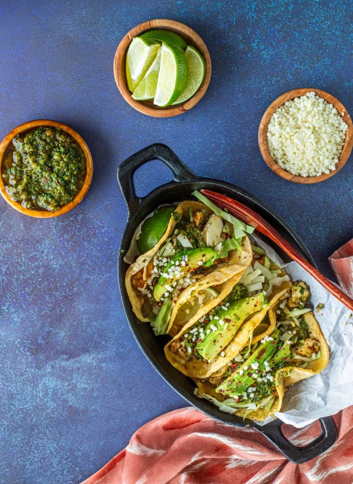A cast iron plate with 3 chicken chimichurri tacos and toppings.