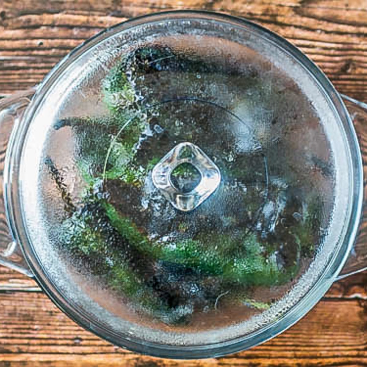 A glass covered casserole with green chiles steaming to loosen blackened skins.