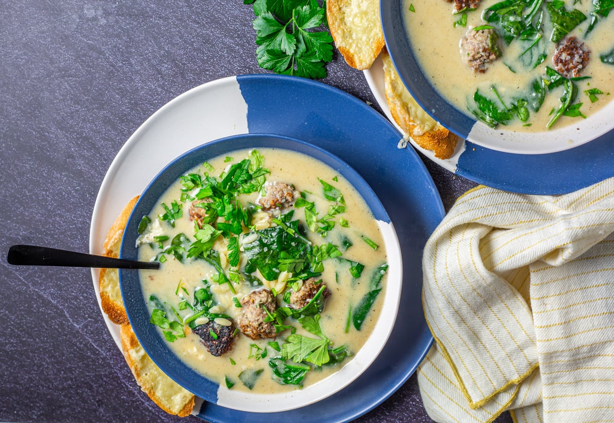 2 bowls of Greek meatball soup with a baguette, glass of red wine, linen napkin.