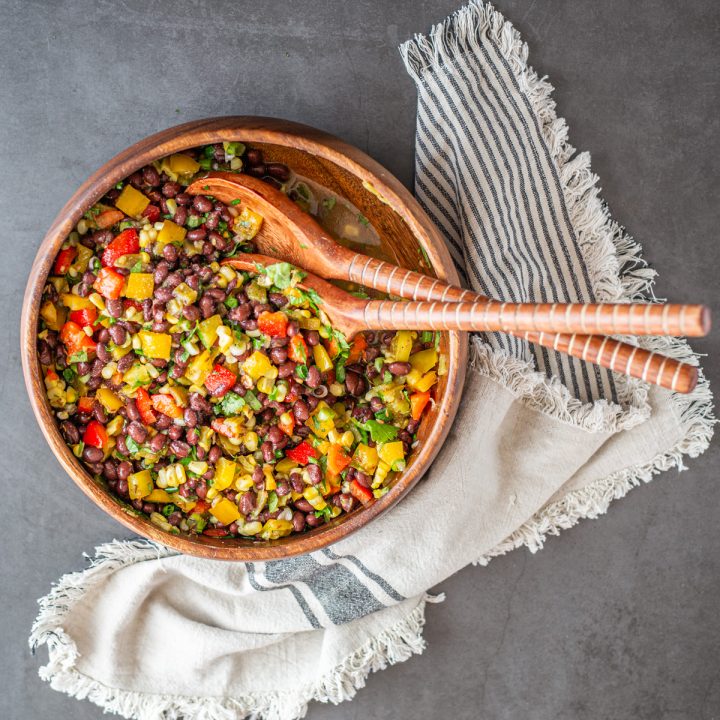 A wood salad bowl with Hatch chile black bean and corn salad with wood salad tools and cloth napkin.