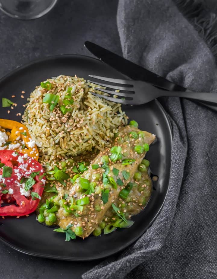 Mexican Salmon in Mole Verde (Pipian) in a black plate with cilantro rice and sliced heirloom tomatoes.