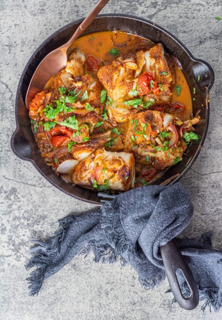 A cast iron skillet with pan-seared Mexican fish and grey cloth napkin.