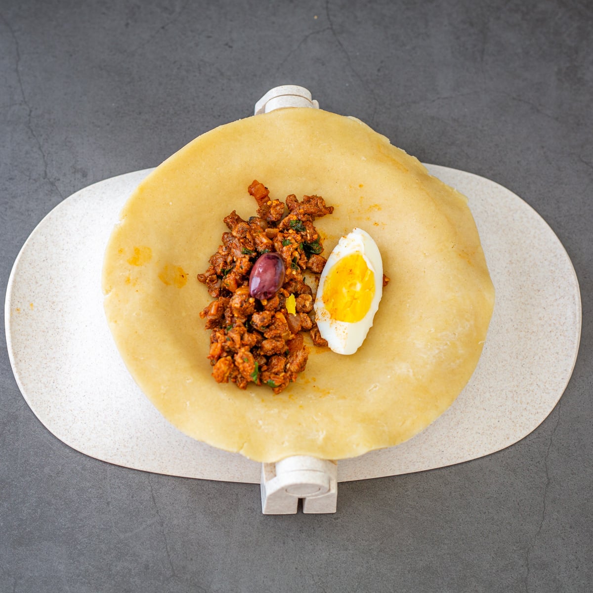 Step 6 - Empanada dough on a press with minced bison/beef, hard-cooked egg, and olive.