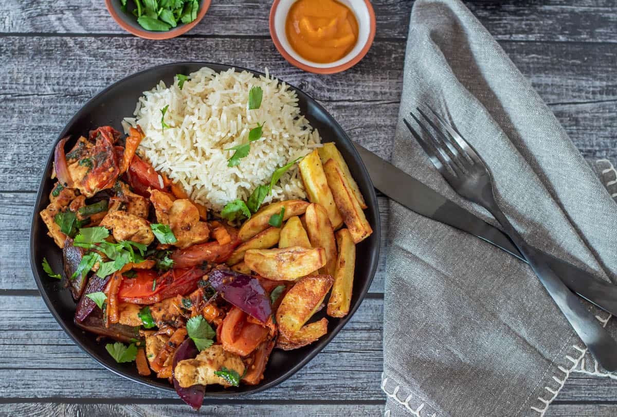 A close up photo of the pollo saltado plated with air fryer potatoes and rice.