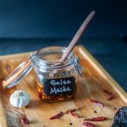 A glass jar with salsa macha on a wood backdrop with dried chiles.