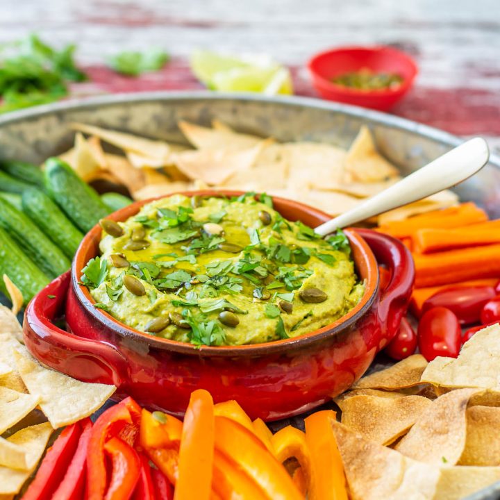 Mexican-Inspired Hummus with Avocado in a clear glass bowl with baked chips.