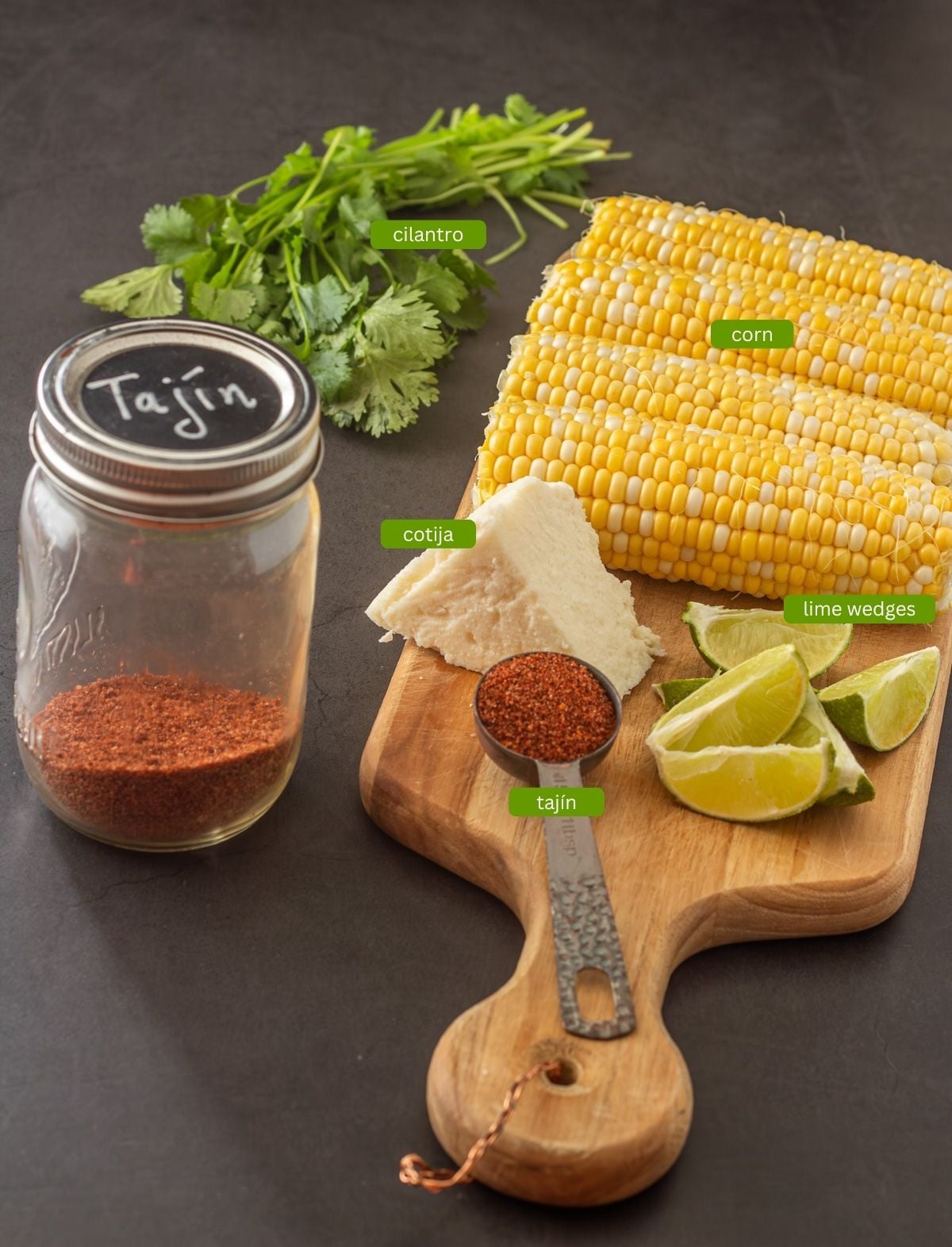 Ingredients for taj&iacute;n corn: Fresh corn, lime wedges, taj&iacute;n, cotija cheese, cilantro.