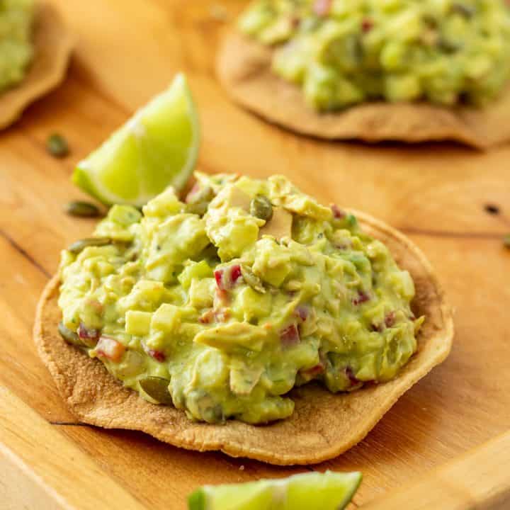 A Mexican tuna salad tostada with lime wedges on a wood tray.