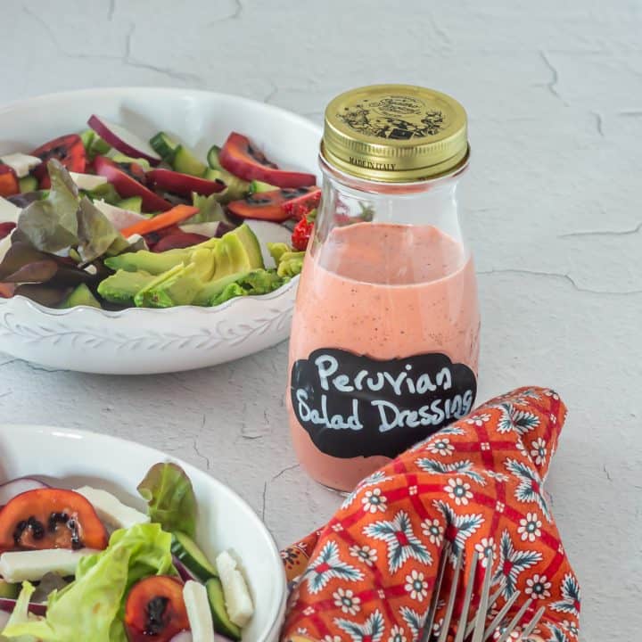 A glass bottle of homemade fresh strawberry/fresas frescas vinaigrette with 2 bowls of salad.