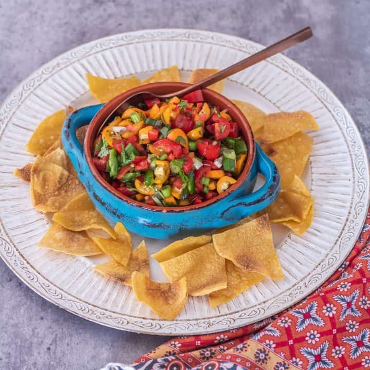 Fresh kumquat salsa with tomatoes and peppers in a turquoise stoneware bowl with tortilla chips.