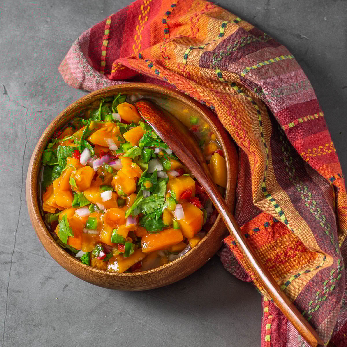 A wood bowl filled with tamarillo/tree tomato salsa, wood spoon, bright napkin.