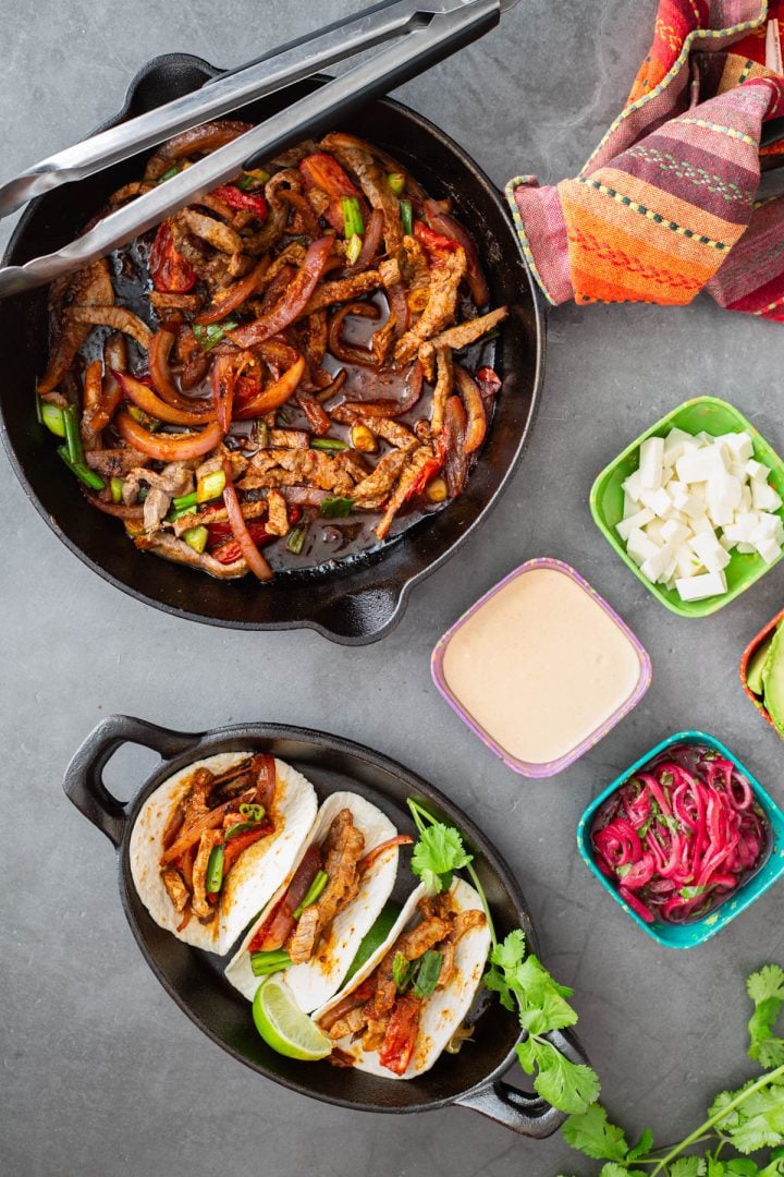 A cast iron skillet of lomo saltado for fusion lomo saltado tacos with toppings.