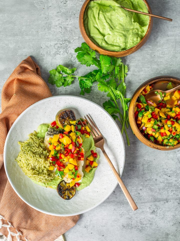A serving of Mexican sea bass with avocado crema and mango salsa on a white plate.