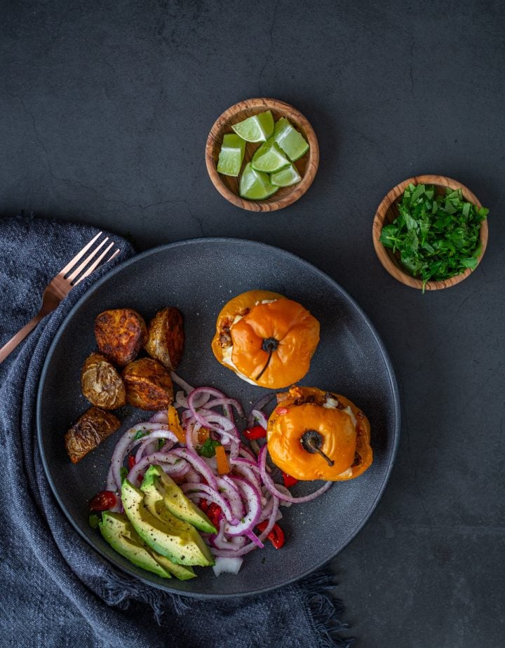 Two rocotos rellenos on a black plate with salsa criolla and Peruvian potatoes.