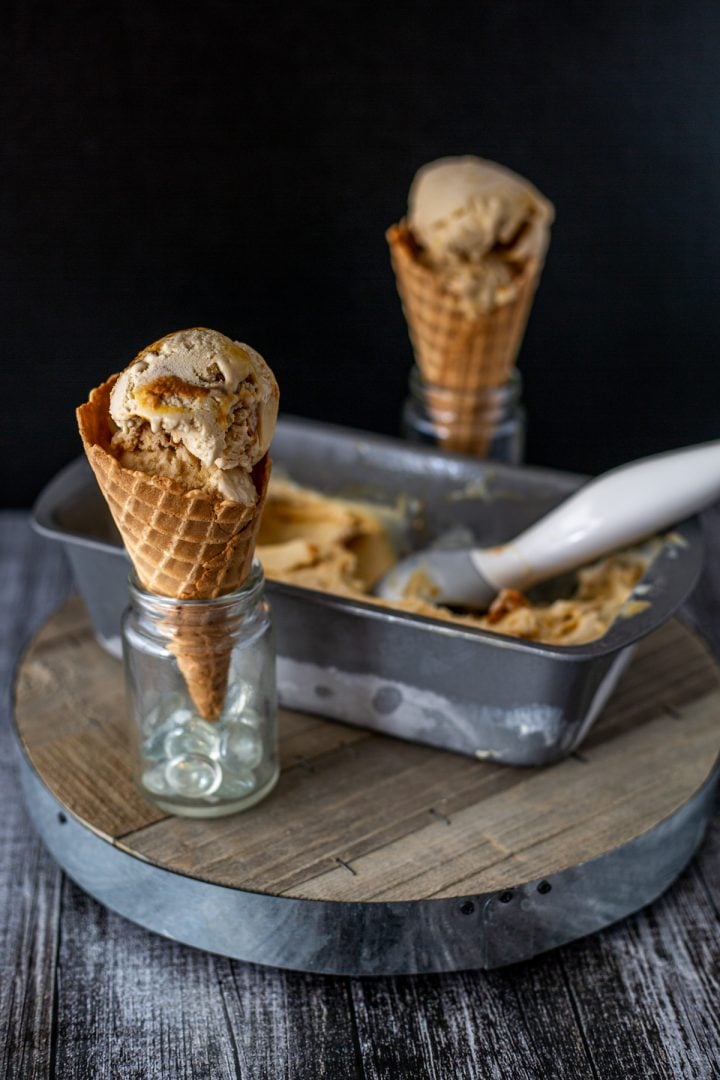 2 waffle cones with dulce le leche ice cream and a loaf pan with ice cream and scoop.