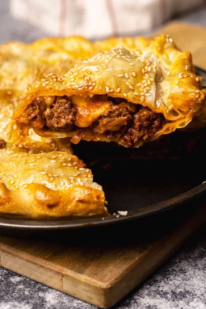 Pastry filled with ground lamb pie on a bronze plate on top of a wood cutting board.