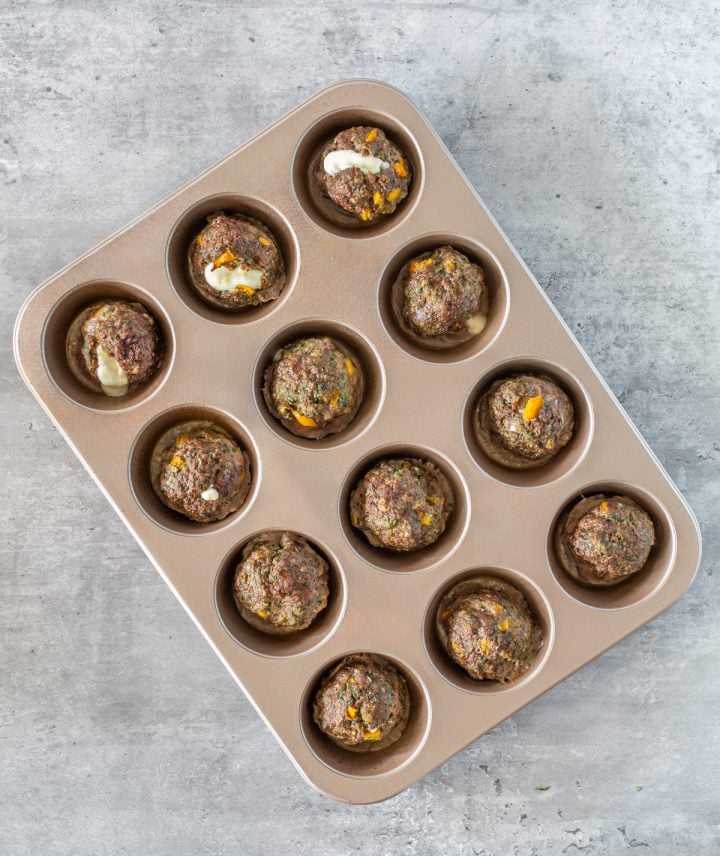A muffin pan with 12 Peruvian cheese stuffed meatballs.