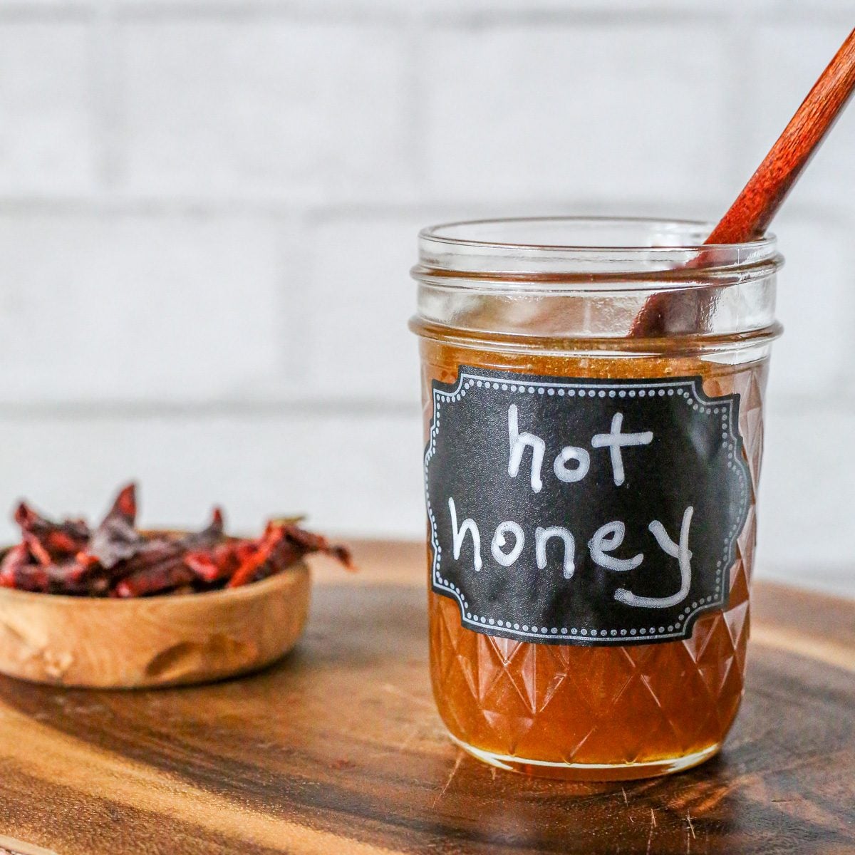 A wood cutting board with a jar of hot honey.
