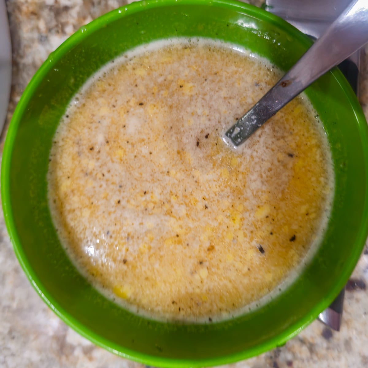Eggs are tempered with hot broth in a green bowl.