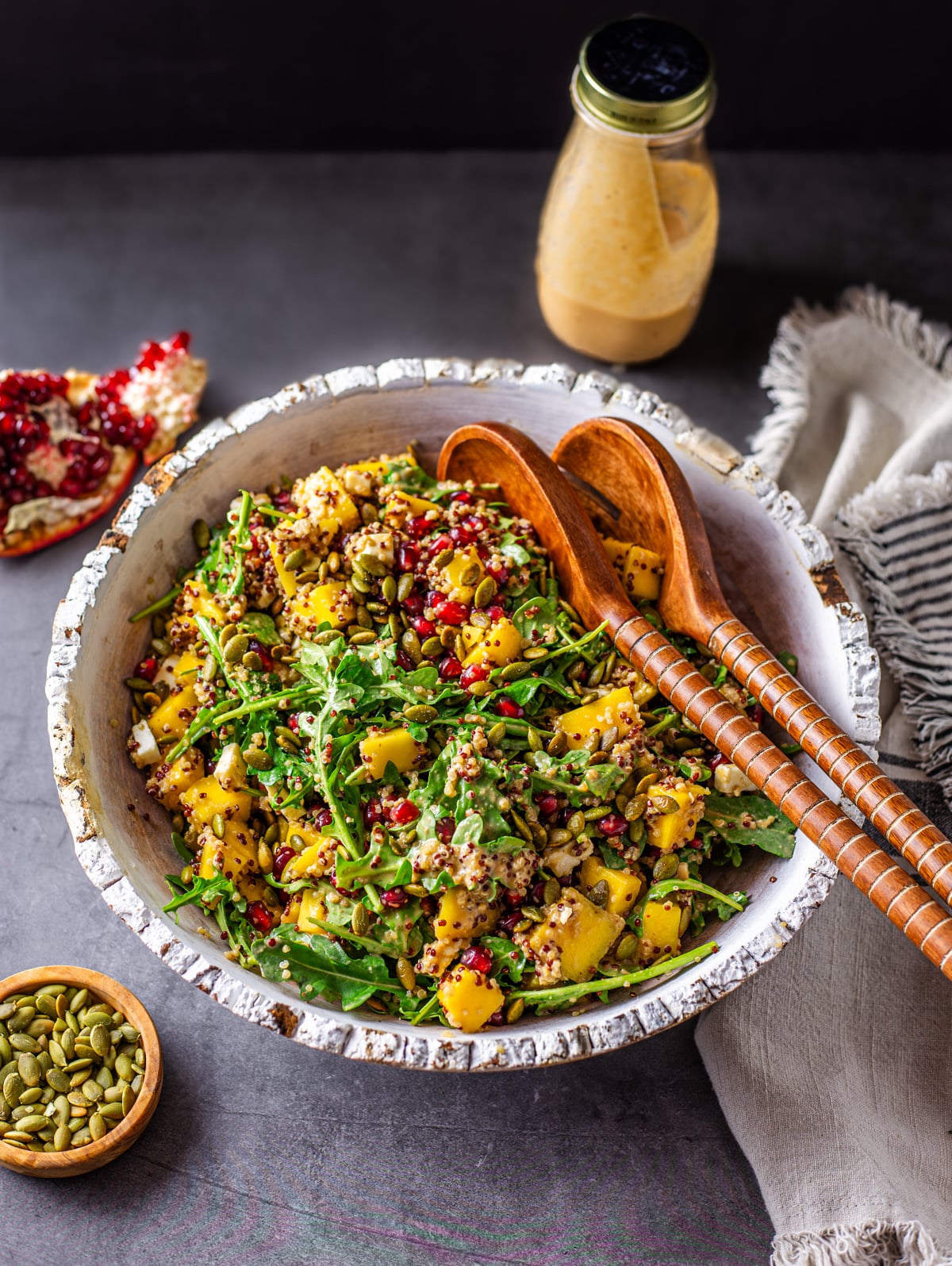 A rustic white bowl with the arugula and quinoa salad tossed with pomegranate vinaigrette.