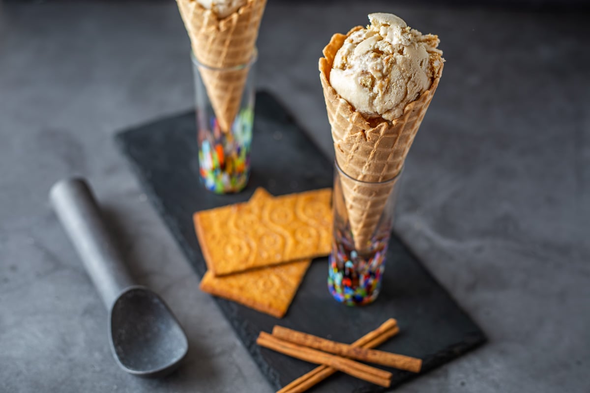 A slate tray with 2 cinnamon ice cream cones, cinnamon cookies, cinnamon sticks, and scoop.