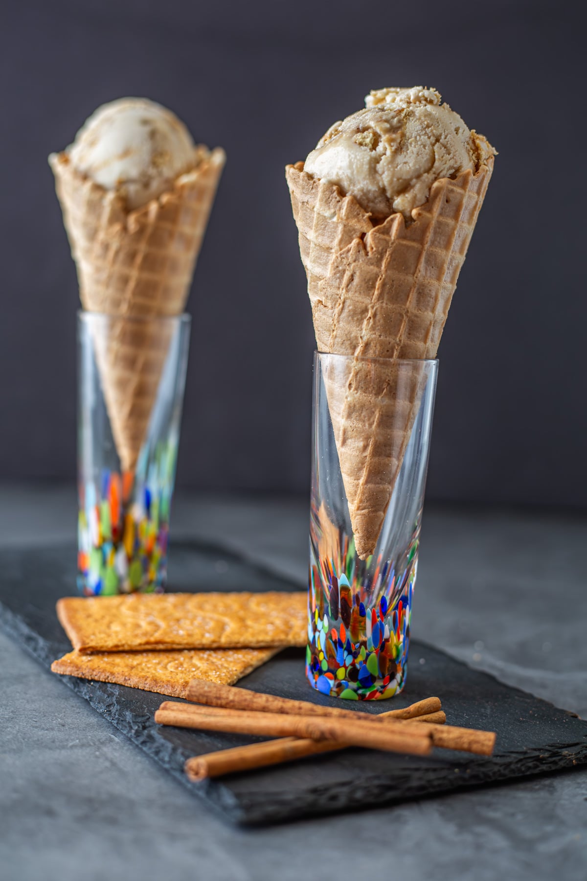 2 colorful glasses with waffle cones with cinnamon frozen custard on a slate tray.