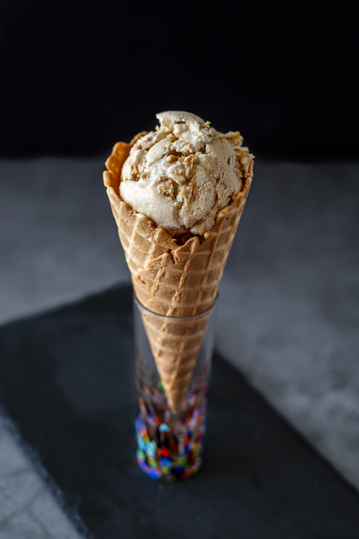 A single scoop of custard-style cinnamon ice cream in a colorful glass on a slate tray.