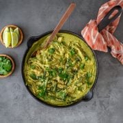 Creamy poblano chicken and peppers in a cast iron skillet with lime wedges and cilantro.