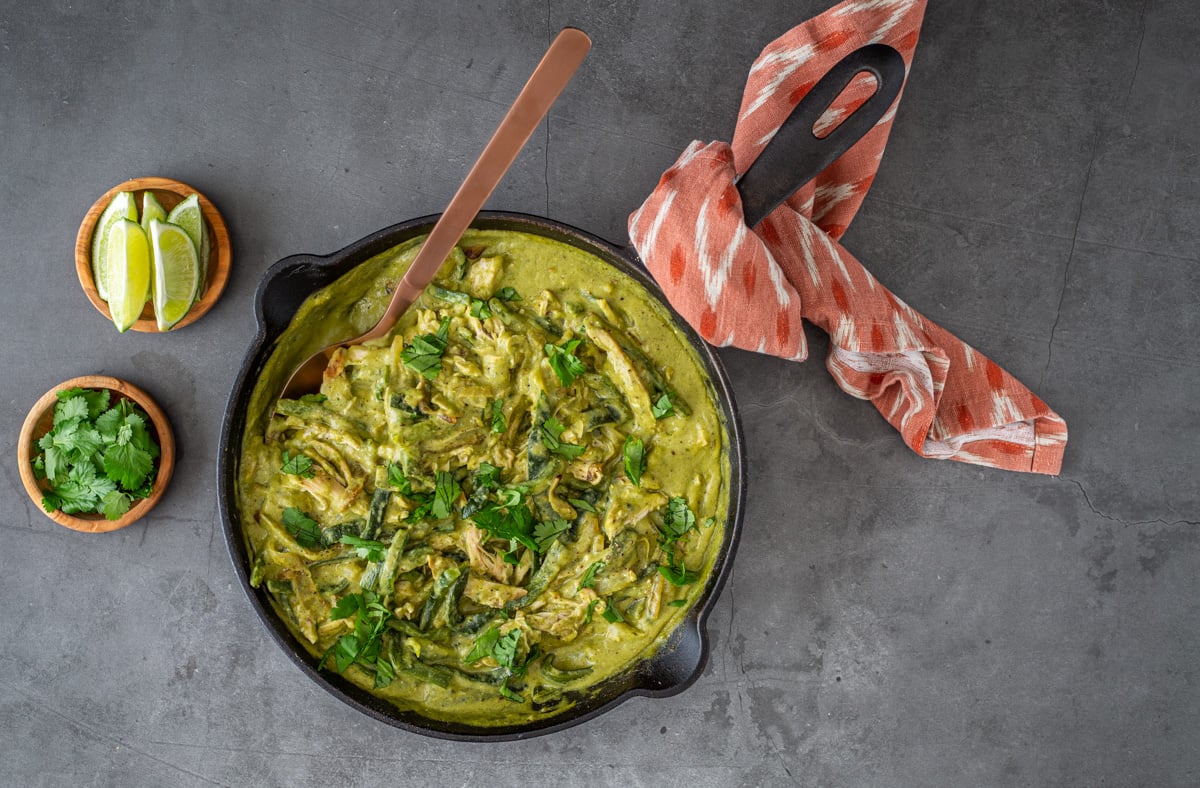A close up of a cast iron skillet with the completed creamy poblano chicken garnished with cilantro and lime wedges.