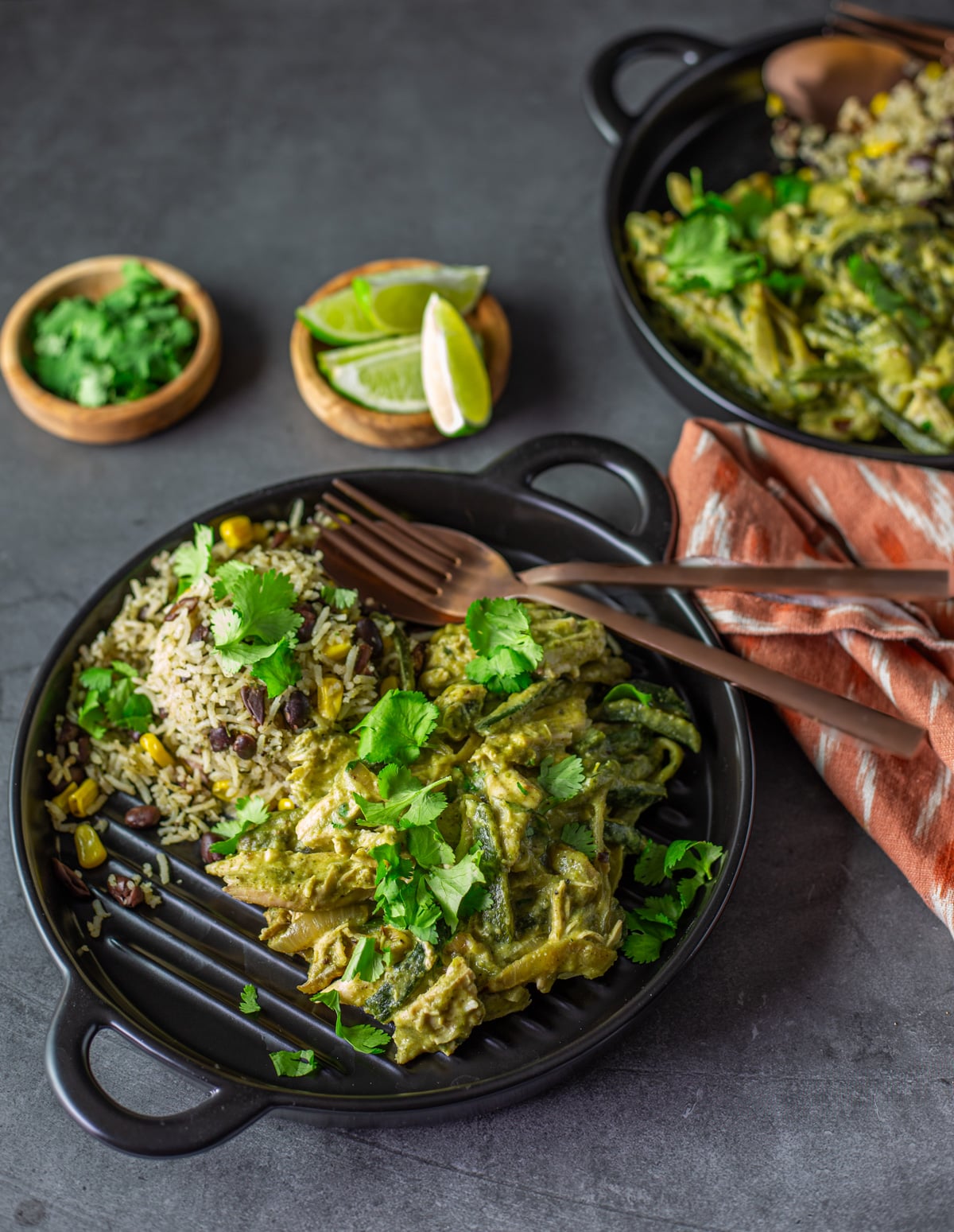 A black stoneware plate with the spicy Mexican chicken alongside cilantro rice with lime wedges and cilantro.