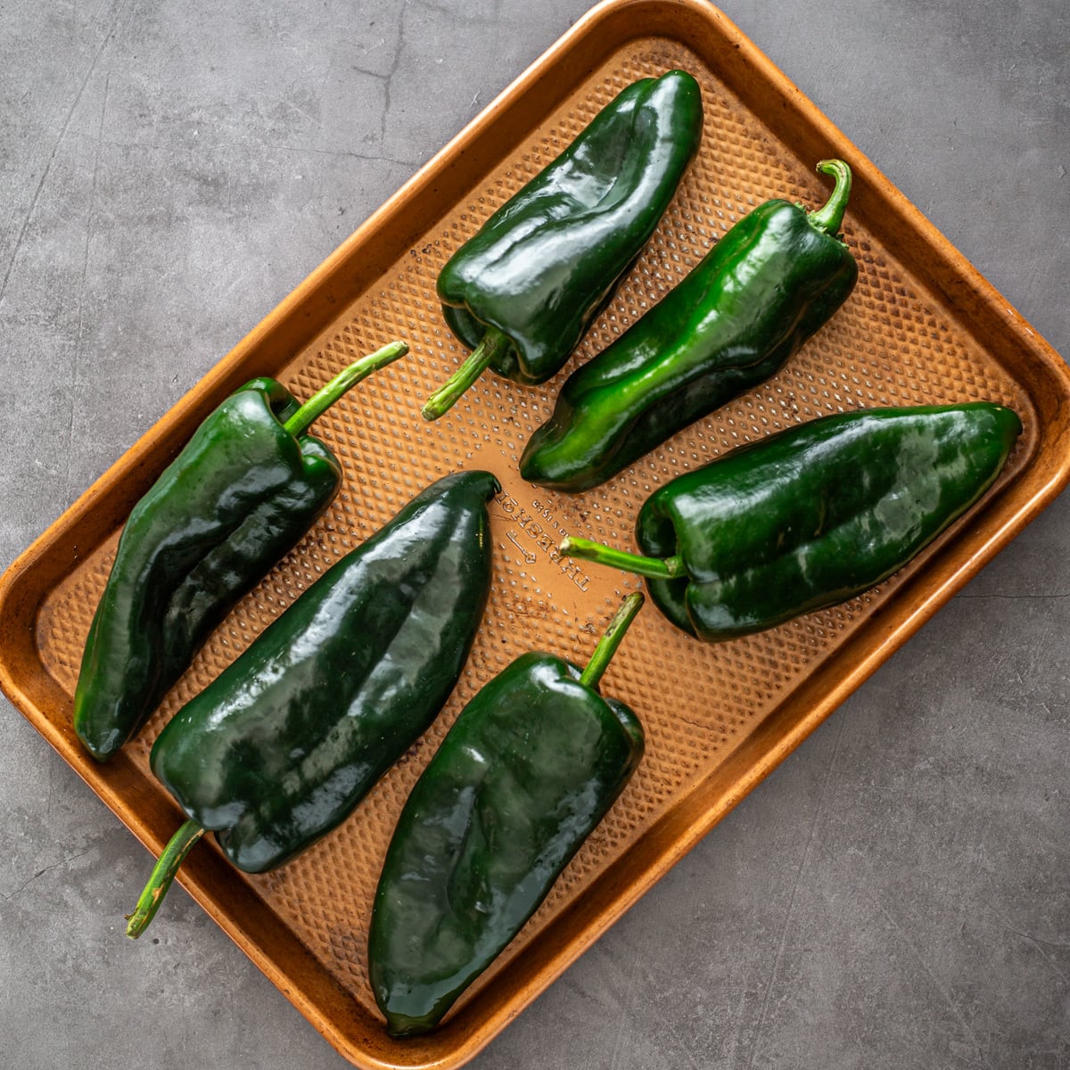 6 poblano peppers on a copper baking sheet before cooking.