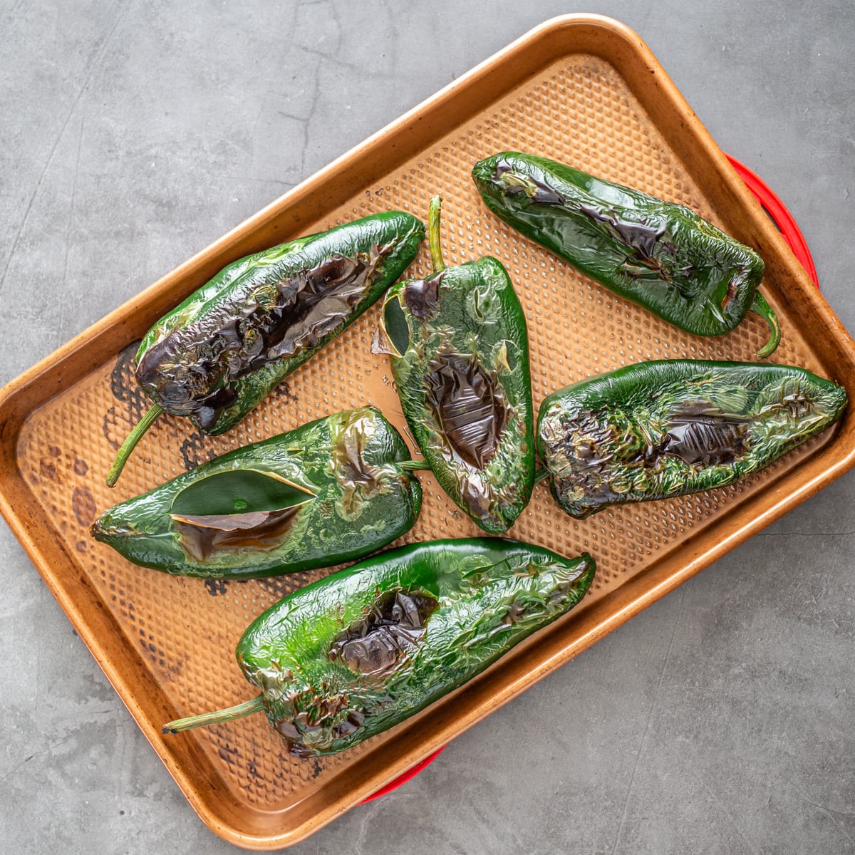 6 charred poblano peppers after they're broiled on a copper baking sheet.
